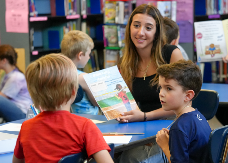 Students reads book to younger students